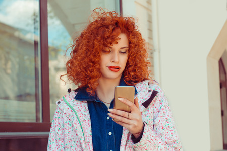 A bored young woman is using a smartphone outdoors in the street. Negative human emotions face expression feelingの写真素材