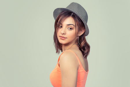 Woman looking back camera confused jealous, teenage hipster girl in gray hat posing turning back isolated light green studio wall background. Positive face expression, human emotion.の写真素材