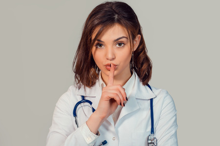 Doctor, woman in white robe showing hush sign gesture with hand isolated on light green backgroundの写真素材