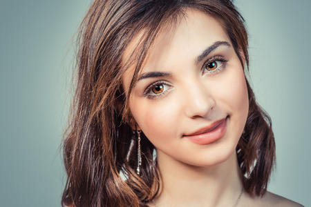 Natural beauty. Closeup portrait cropped image on the face head of a woman cute brunette teenage girl looking at you smiling isolated light green blue studio wall background. Positive face expressionの写真素材