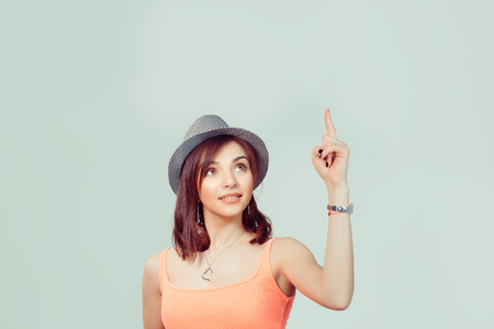 Look up here. Beautiful funny confused woman presenting showing copy space above head with index finger hand isolated light green yellow background. Beauty bob hair style with gray hat on headの写真素材