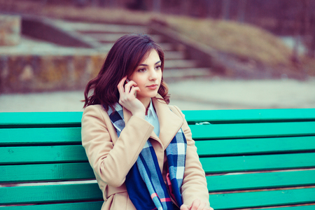 Phone talk outside. Russian asian girl, American woman outside sitting on a bench talking at cellphoneの写真素材