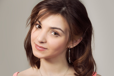 Natural beauty. Closeup portrait cropped image on the face head of a woman cute brunette teenage girl looking at you smiling isolated light beige studio wall background. Positive face expressionの写真素材