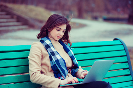 Russian asian girl, mixed race American woman outside sitting on a bench using laptop, outdoors in a city park.の写真素材