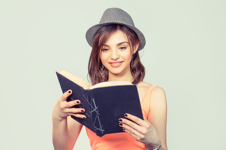 Girl with book. Closeup beautiful young woman pretty happy reading, hipster girl in pink shirt holding black notebook isolated light green background wall. Bob hairstyle, love the romance, positive emotionの写真素材
