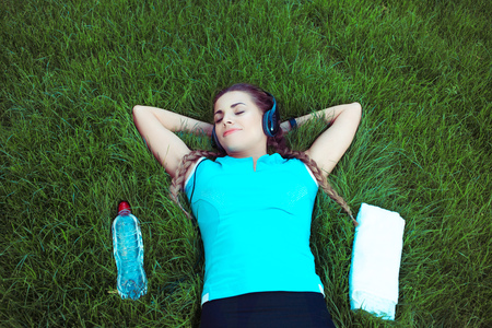 From above of young fit sportswoman lying on green lawn with bottle of water and towel, in relaxation eyes closed sleeping daydreaming with smile on lipsの写真素材