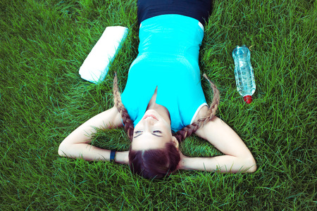 From above shot of young fit sportswoman lying on green grass and listening to music with headphones smiling happyの写真素材