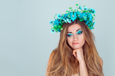 Head shot thoughtful puzzled upset young Woman with floral headband looking down to the side. Fashion girl with crown from sunflowers on head doubtful isolated on light blue background with copyspaceの写真素材