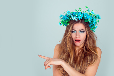 Young shocked sad frustrated, upset, annoyed woman wearing floral headband showing empty copy space pointing with index finger isolated on light blue background. Anemone wreath of flowers on head girlの写真素材