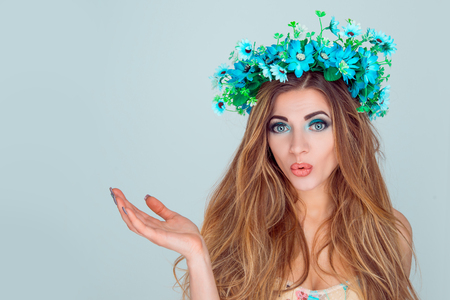Young surprised woman wearing floral headband pointing with open palm to copy space for your beauty product isolated on light blue background. White cherry blossom wreath of flowers on head girlの写真素材