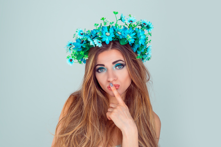 Beautiful young woman wearing anemone floral headband crown isolated on light blue background. with headband from flowers on head looking at you camera with puzzled and interested, thoughtful lookの写真素材