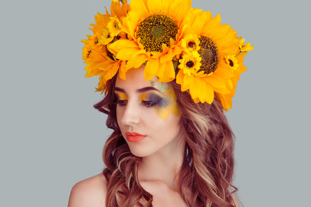 Beautiful young beautiful woman beauty model with yellow sunflowers head floral headband eyes closed looking down shows makeup posing looking down isolated on gray background. Spring style concept.の写真素材