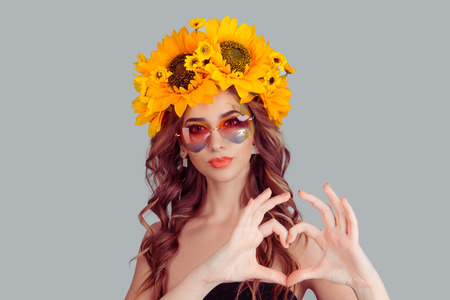 Woman in sunflowers floral headband wearing heart shaped sunglasses over isolated gray background smiling puckering lips in love showing heart symbol and shape with hands. Romantic Valentine concept.の写真素材