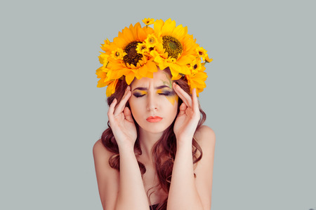 Stressed beautiful woman with floral headband touching temples thinking hard. Young lady having headache. Stress or headache concept isolated front view on gray Fashion girl with crown from sunflowersの写真素材