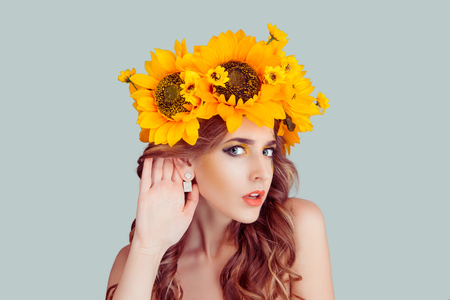 Woman with floral headband hand to ear listening in shock. Closeup portrait of Noisy Caucasian Fashion girl with crown from sunflowers on head hand to ear isolated on gray background with copy space.の写真素材