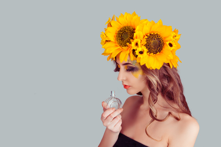 Beautiful sensual Woman with floral headband holding perfume bottle smelling aroma. Fashion girl with crown from sunflowers on head isolated on gray background with copy space. Excellent odor smell.の写真素材