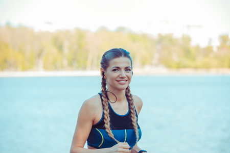 Portrait charming attractive young woman in sportswear at training in sunny morning on seafront urban background.の写真素材