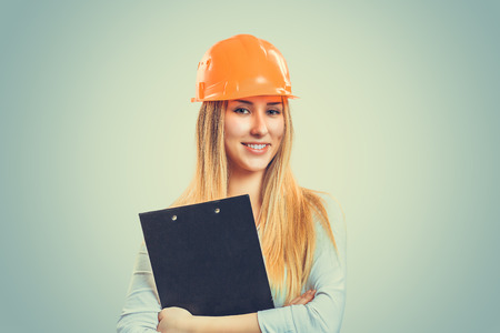Professional content woman in white shirt wearing orange hardhat and holding clipboard. Caucasian Business person in white formal shirt, blonde hair isolated on light green yellow studio background.の写真素材