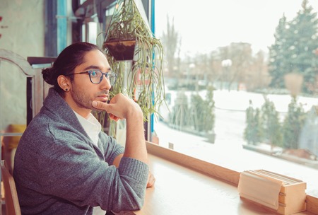 Man in living room looking through window, being thoughtful.