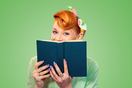 beautiful happy smiling woman pinup retro hair style girl hiding herself behind a book isolated green background copy spaceの写真素材