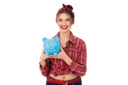 Joyous happy young woman 20s in casual clothing holding blue piggy bank with lots of money isolated over white backgroundの写真素材