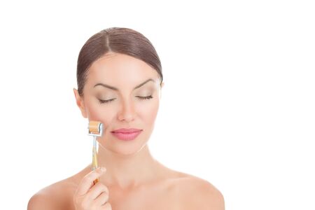 Beauty girl using derma roller. Close up portrait smiling cute beautiful woman, showing mezo-roller, for clean skin fresh face, eyes closed, nude body isolated on white background with copy spaceの写真素材