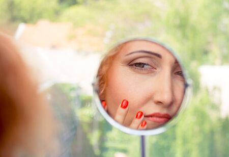 Woman looking, examining her nasolabial fold, her first signs of aging. Beauty and skincare concept of a mature woman.の写真素材