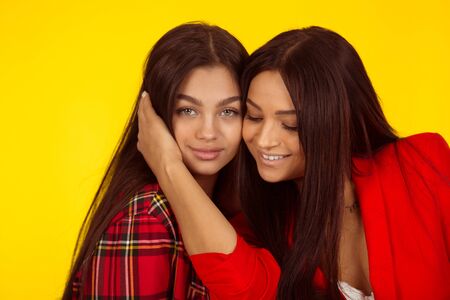 Mother hugging her daughter and smiling wearing red outfits. Mixed race model isolated on yellow background with copy space. Horizontal image.の写真素材