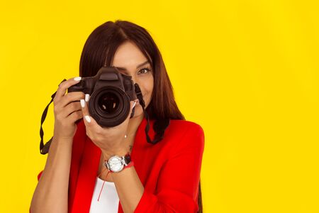 young woman taking pictures with professional camera. Mixed race model isolated on yellow background with copy space. Horizontal image. Natural, no makeup.の写真素材