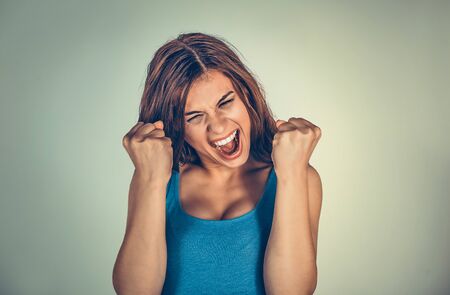 Excited woman holding fists up in triumph celebrating win and looking up happily. Mixed race model isolated on light green background with copy space. Horizontal image.の写真素材