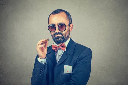 Ace card under sleeve - business man. Serious bearded boss in sunglasses, holding a cigar in hand with ace in his pocket isolated on gray background. Secret. Success, winner. Backup strategy concept.の写真素材