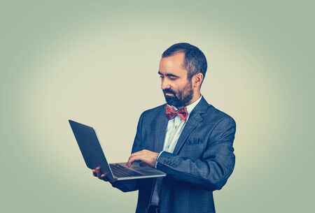 Young handsome mature middle age business man connecting to internet using looking attentively in a laptop. Mixed race bearded guy isolated on green studio wall background with copy space. Horizontalの写真素材