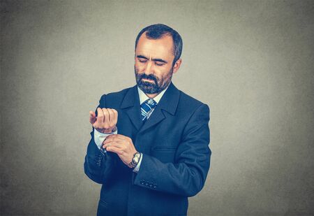 Half body portrait of handsome bearded man in formal wear fastens cufflinks, the buttons of his...