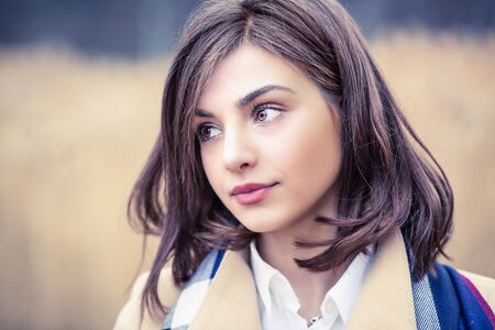 Pretty Woman looking to the side away thinking beige coat in autumn Outdoors park backgroundの写真素材