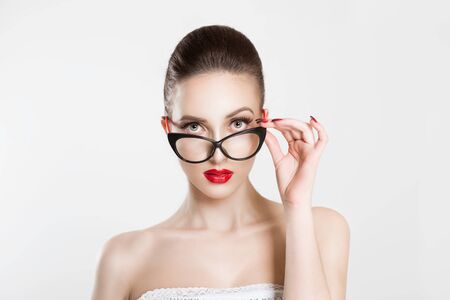 Portrait of beautiful skeptical woman in stylish cat eye eyeglasses, thinking and looking at you with disapproval. Holding her eye-wear glasses with her hand. Negative face expression, body languageの写真素材