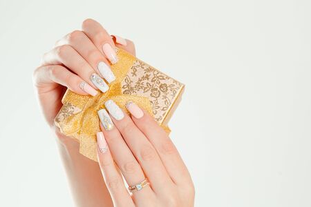Gift box. Modern style pastel coral pink white wedding Nail Polish. Beauty hands holding golden gift box. Stylish Colorful french Nails isolated white background.  Nail Polish. Art Manicure.の写真素材