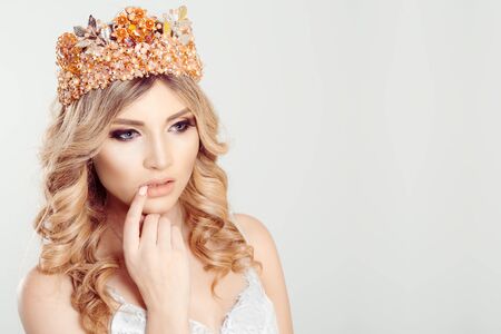 Sad thoughtful beauty woman. Closeup pensive thinking woman looking down with white gold diamond crown on head, curly long blonde hair isolated white gray backgroundの写真素材