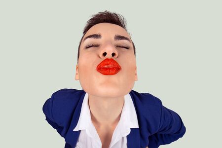 First kiss, unwanted kiss concept. Closeup portrait of nerdy young funny distorted woman face with big red lips eyes closed trying to kiss you camera, isolated light green white backgroundの写真素材