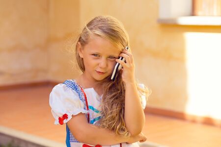 Cute little girl child explains to his parents how she spent the day upset looking at you camera isolated near house external wall outdoors backgroundの写真素材