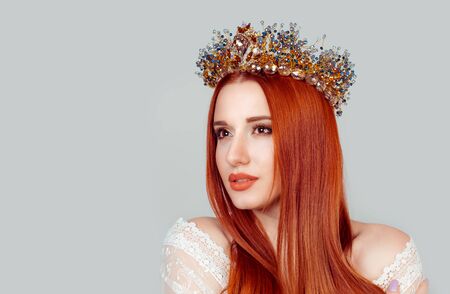 Beautiful girl in a golden crown on grey background, looking to the side hopeful with daydreaming look smiling happy pretty woman with crystal crown on head isolated on light gray background wallの写真素材