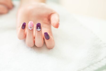 Beautiful colored beige burgundy red pastel colors nail polish with gem crystal stones on hand, closeup. Nail art manicure conceptの写真素材
