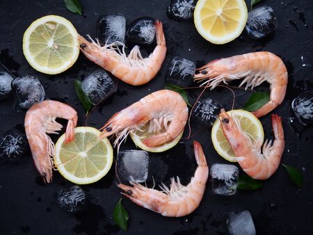 Fresh shrimps with rosemary or basil spices, lemon and ice on a black stone board plate as a background. Top view of seafood ingredients.の写真素材
