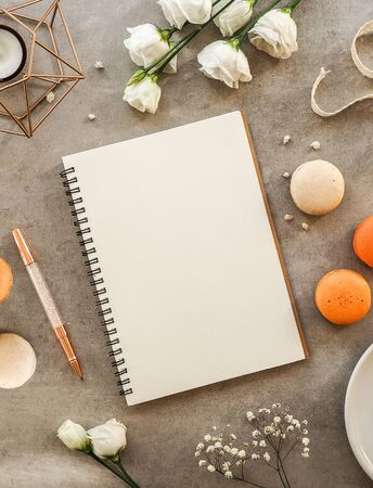 French orange and beige macaroon cakes, white gypsophilas and roses flowers, pen and notebook for recipes flowers on gray stone background. Flat lay, top view. Top view flat lay, vertical imageの写真素材