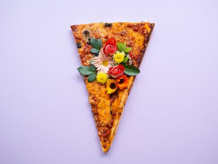 Slice of pizza isolated on a purple background with spring flowers on it. Piece of pizza with a bouquet of red yellow orange white flowers of lilac, tulip, chrysanthemum and roses with green leaves.の写真素材
