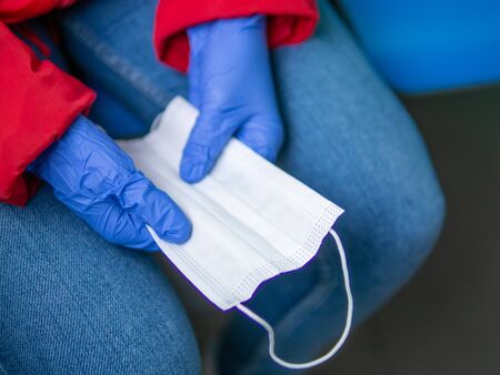 A woman hands in blue rubber gloves holding spare surgical mask protecting from viruses in public transportation. Covid-2019 pandemic conceptの写真素材