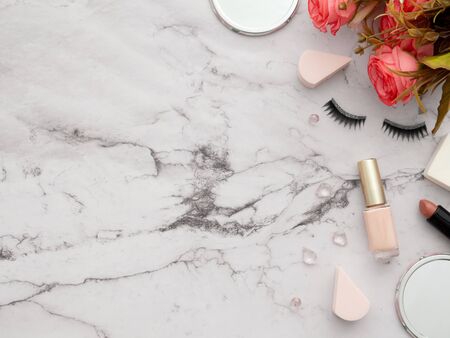 Female fashion beauty blogger workspace. Makeup tools cosmetics, false eyelashes, mirrors, lipstick, sponges, nail polish, roses flowers isolated on marble table with copy space background. Top viewの写真素材