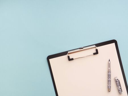 Clipboard with white sheet and pen isolated on a blue color background. View from above, flat lay,...