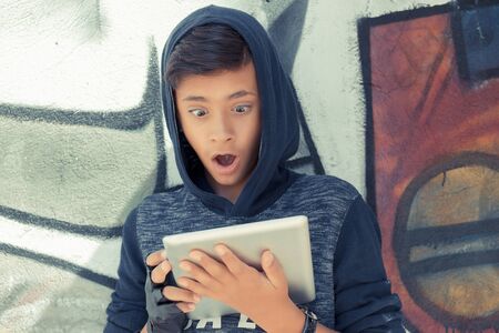 Surprised boy looking at the tablet pad isolated graffiti wall background