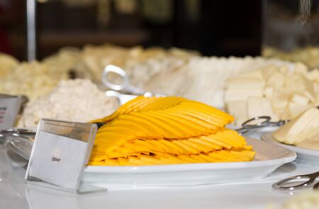 Cheddar cheese slices on white plate, different blurred other kind of cheese on backgroundの写真素材