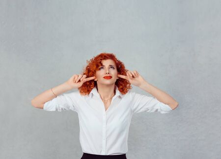 Occlude the ears. Closeup portrait young angry unhappy stressed redhead curly woman covering plugging her ears looking up, stop making loud noise it's giving me headache isolated gray wall backgroundの写真素材